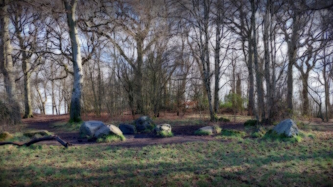 Camphill stones: A dream-like image of a group of large boulders on a hilltop with bare trees against a cloudy sky.
