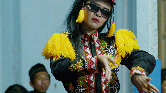 A photo of the artist wearing shades and a brightly coloured and textured costume, the feel is both modern & traditional