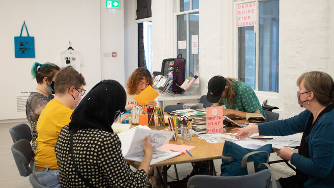 A group of people sitting around a table with collage making materials making zines.