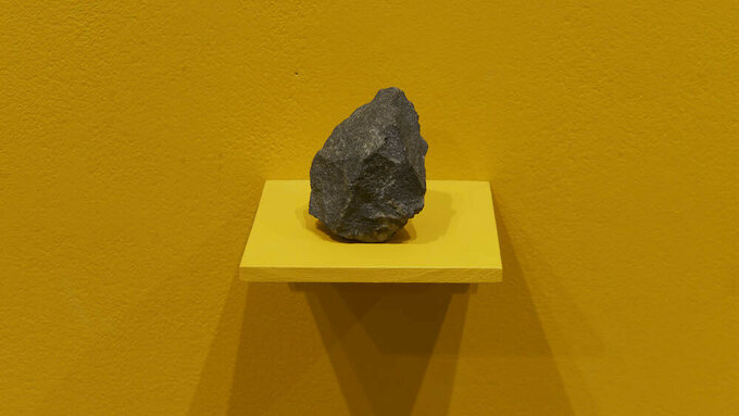 A fist sized piece of dark heavy looking rock, resting on a shelf.
