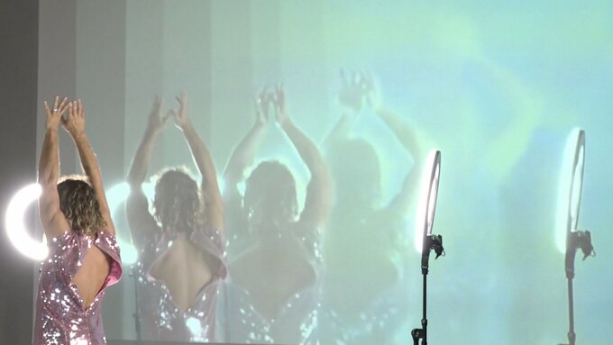 A person in a pink bedazzled dress with their hands in the air, reflected in a series of mirrors.