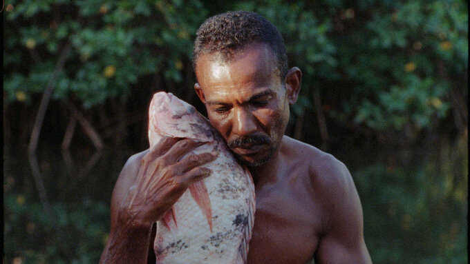 A person with his eyes closed, is holding a caught fish contemplatively close to his body, hands cradling the fish