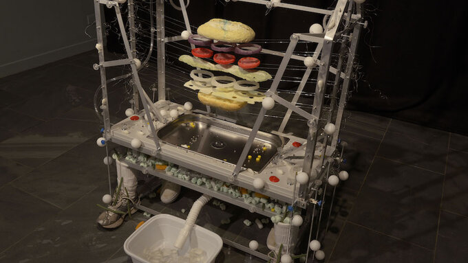A sculpture featuring a dissected sandwich in a large apparatus with a basin of ice and trainers.