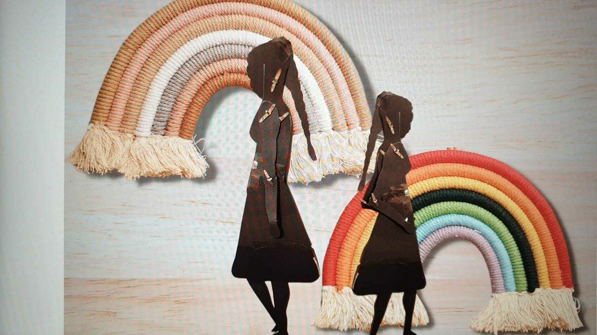 Two black paper cut outs of silhouettes of two women with braids. These are pasted on rainbows made from woven fabric