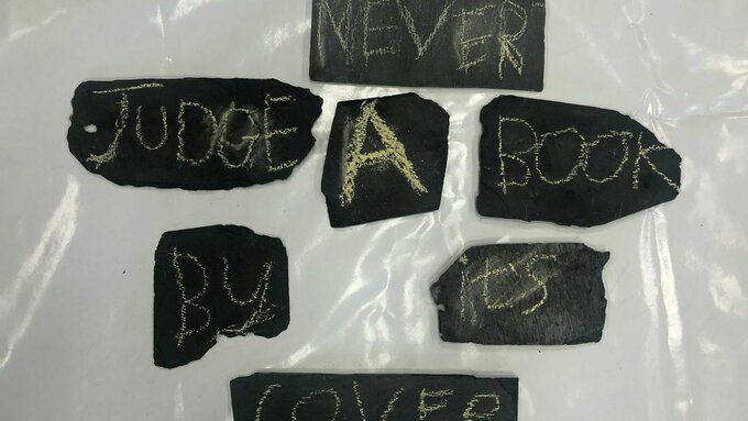 A number of black slates each with a single chalk word which reads "never judge a book by its cover"
