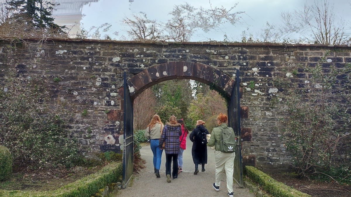 Five women walking under a stone arch are seen from behind