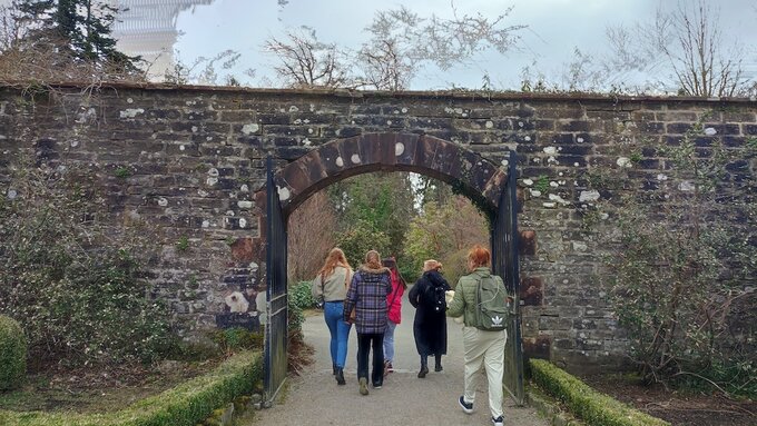 Five women walking under a stone arch are seen from behind