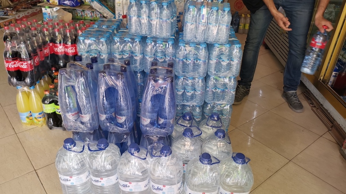 Plastic water bottles are stacked together in a shop. A person leans down near them.