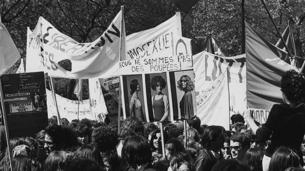 A black and white photo of a crowd or protesters holding placards, signs, and flags.