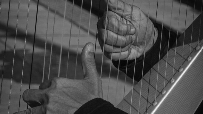 Close up in black and white of old hands playing a harp