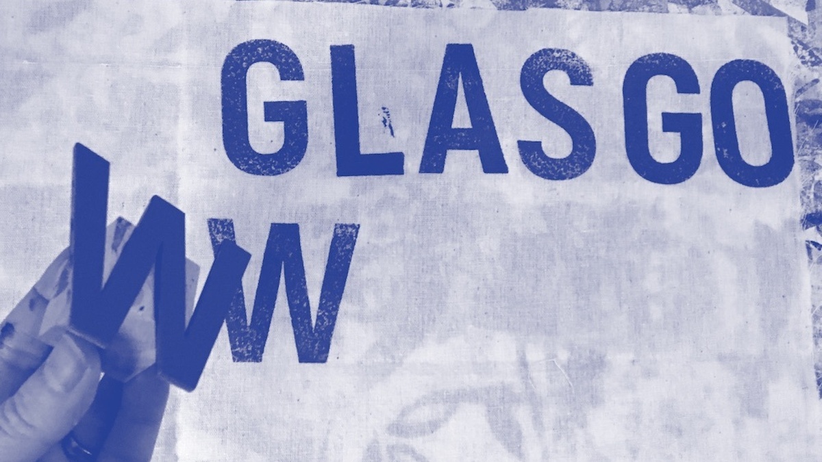 Glasgow printed on to fabric with a hand holding the W that has been printed.