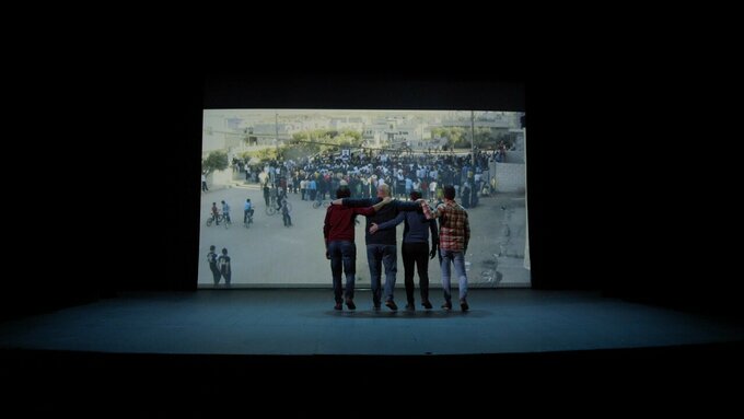 Four men stood on a stage in front of a screen displaying an image of a large group of people gathering.