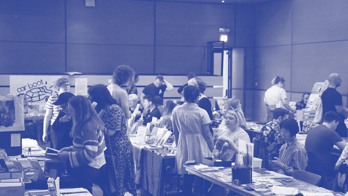 The zine fair in the theatre at CCA - rows of tables with zines on with people looking and chatting around them.