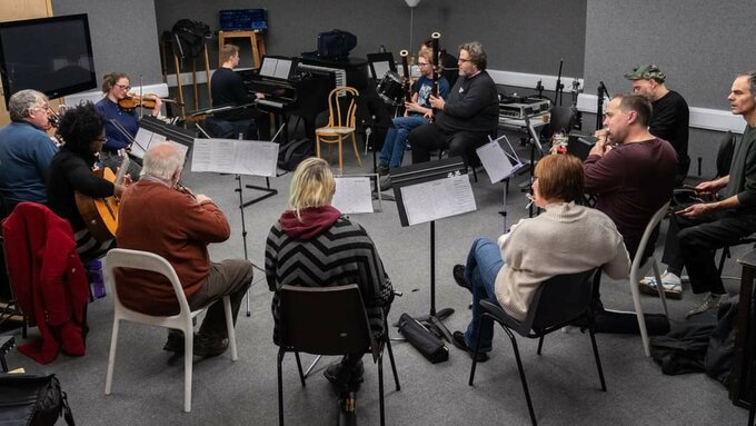 Casually dressed people sitting in a circle, holding their instruments in their lap, some playing, some discussing