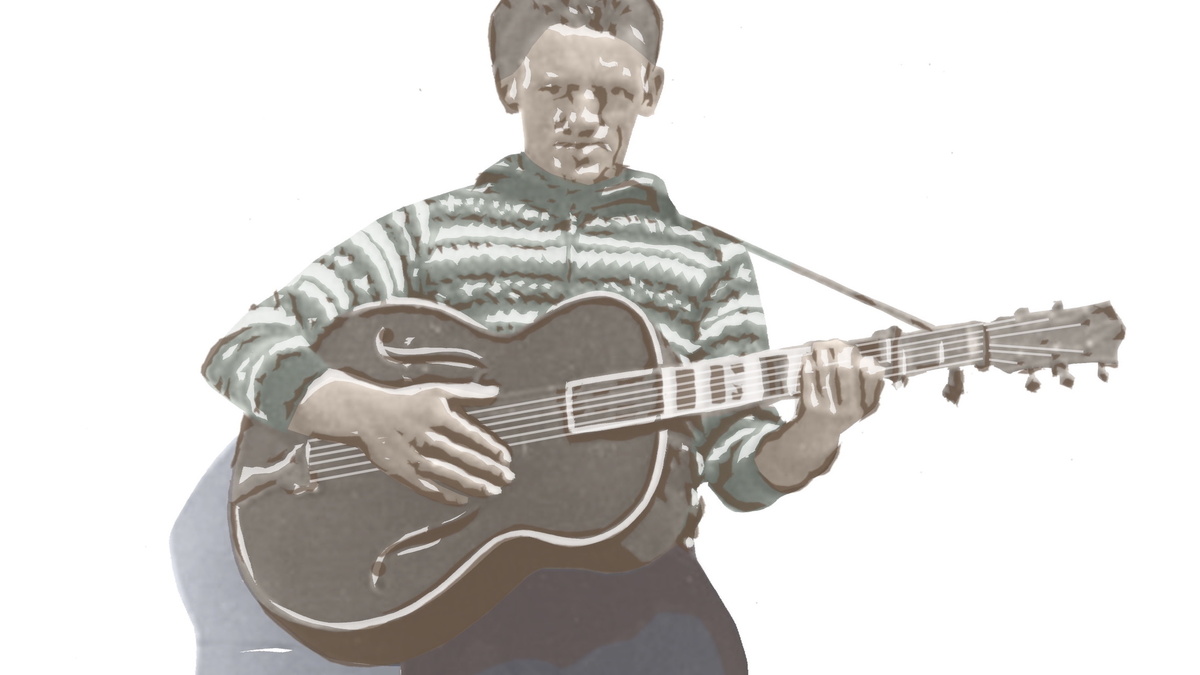 A man is standing in bright sunlight holding an acoustic guitar and wearing a Fair Isle jumper.