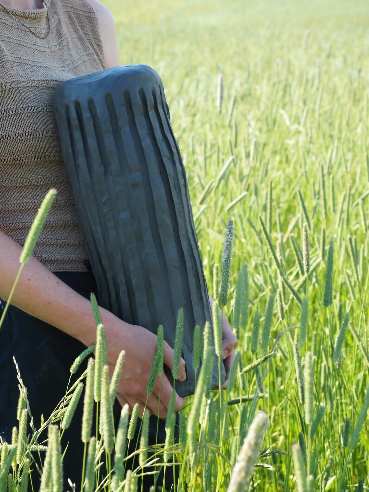 A photo of someone holding an un-baked clay column in a field of tall grass