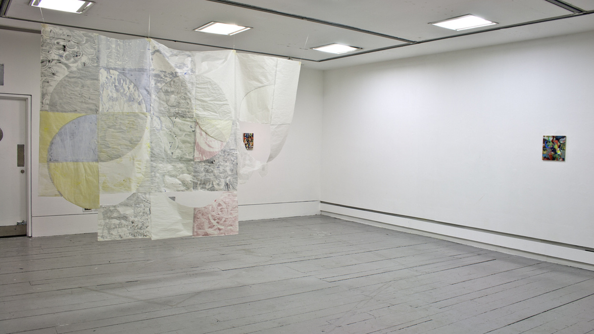 Install view of the show, a geometric quilt hangs from the ceiling and a small painting sits on the far right wall.