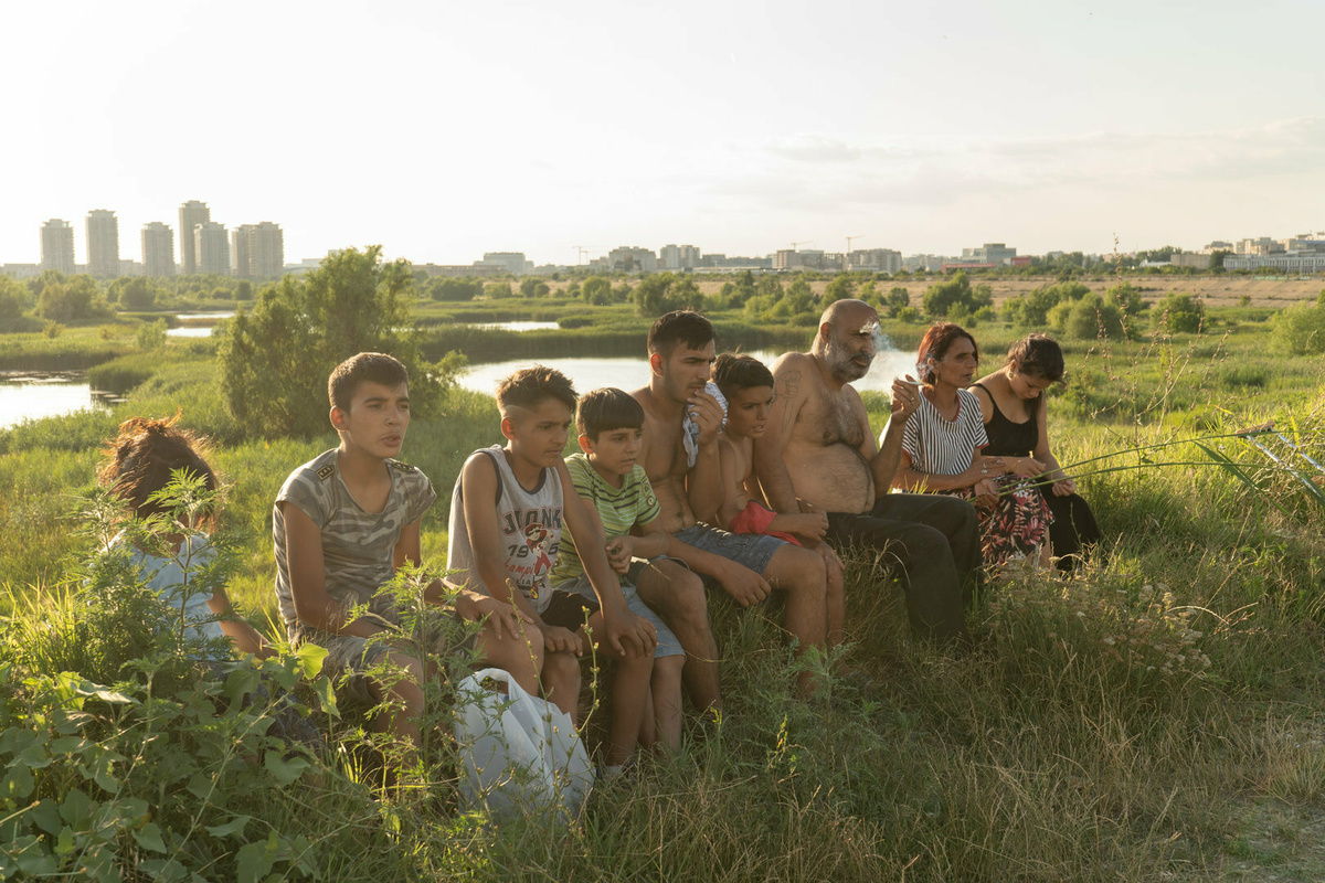 A family of nine, sitting in a green field, with high-rises in the background.