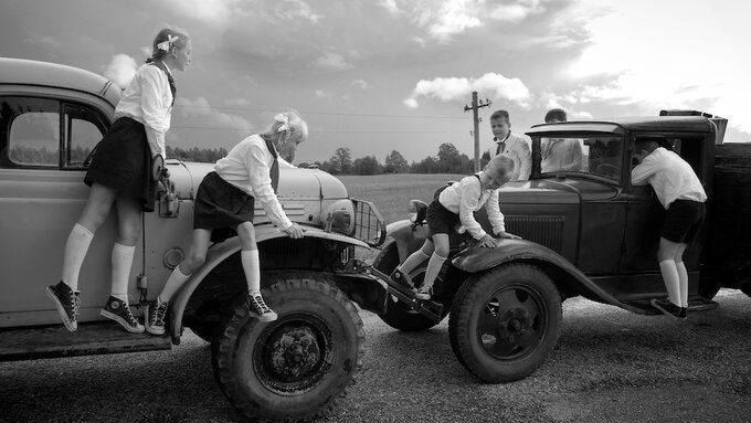 A B&W shot of six children, wearing soviet pioneer (equivalent of boy scout) clothing, climbing on two trucks.