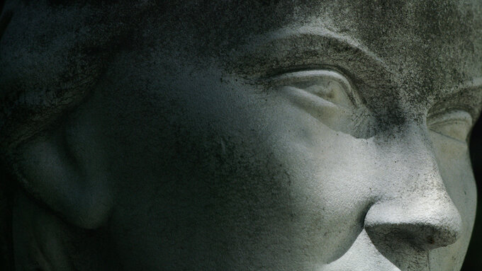 A close-up of the eyeline of a faded statue, against a completely dark background.