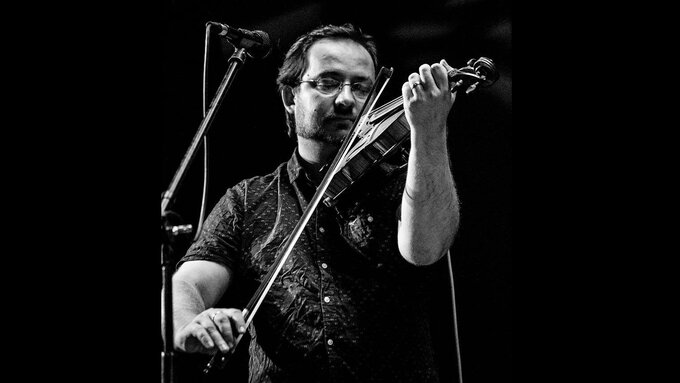 A black and white photo of Jani Lang playing a violin with his eyes closed and a serene look on his face.