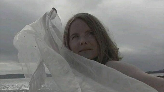 A person with long blonde hair holds a thin white sheet.