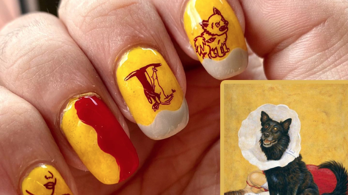 A white hand folded so you can see the fingernails which are painted red and yellow with little images of a wolf.