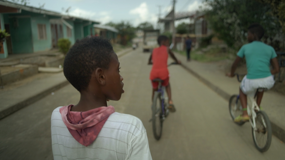 Three Afro-Colombian boys are pictured riding bicycles (facing away from the camera).