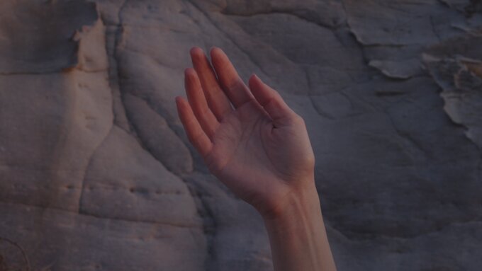 A hand is waving in the air in front of a rock face.