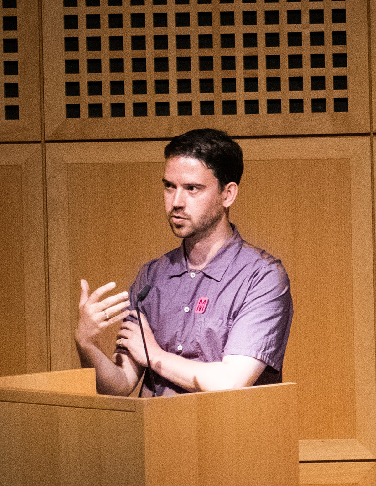 A photograph of Ifor Duncan, he has short black hair, wearing a purple shirt and standing at a podium.