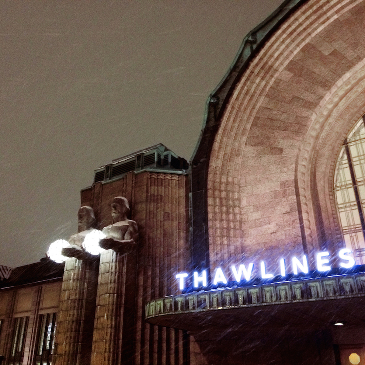 A photograph of a part of a large building, the word "Thawlines" is written on a neon sign.