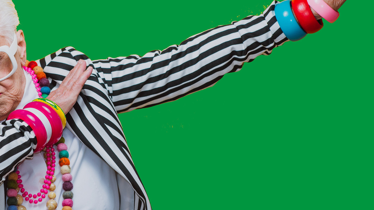 An older woman in a black and white striped jacket strikes a pose against a green background.
