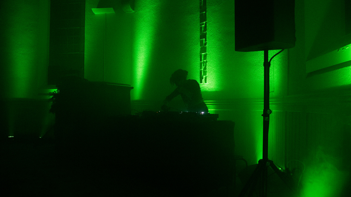 An image of a DJ playing in a smoky room, bathed in green light.