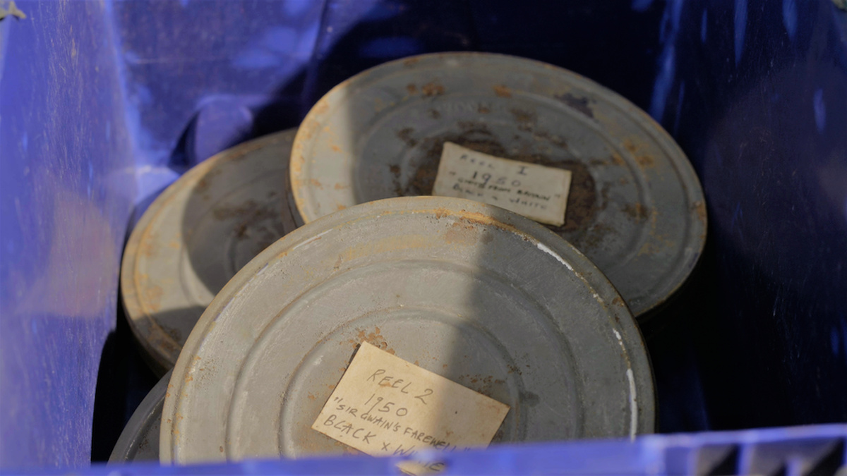 The interior of a well worn blue plastic box holds a number of rusting grey film canisters, labeled with peeling paper.