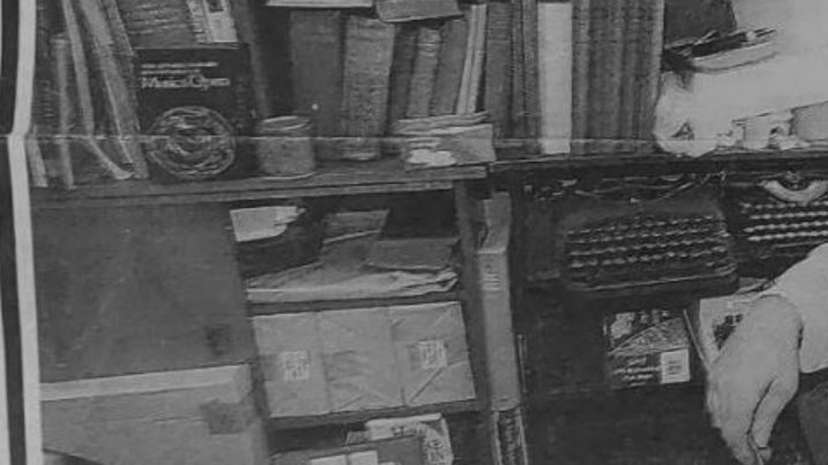 A black and white photo of a dark dusty bookshop full of antique materials.