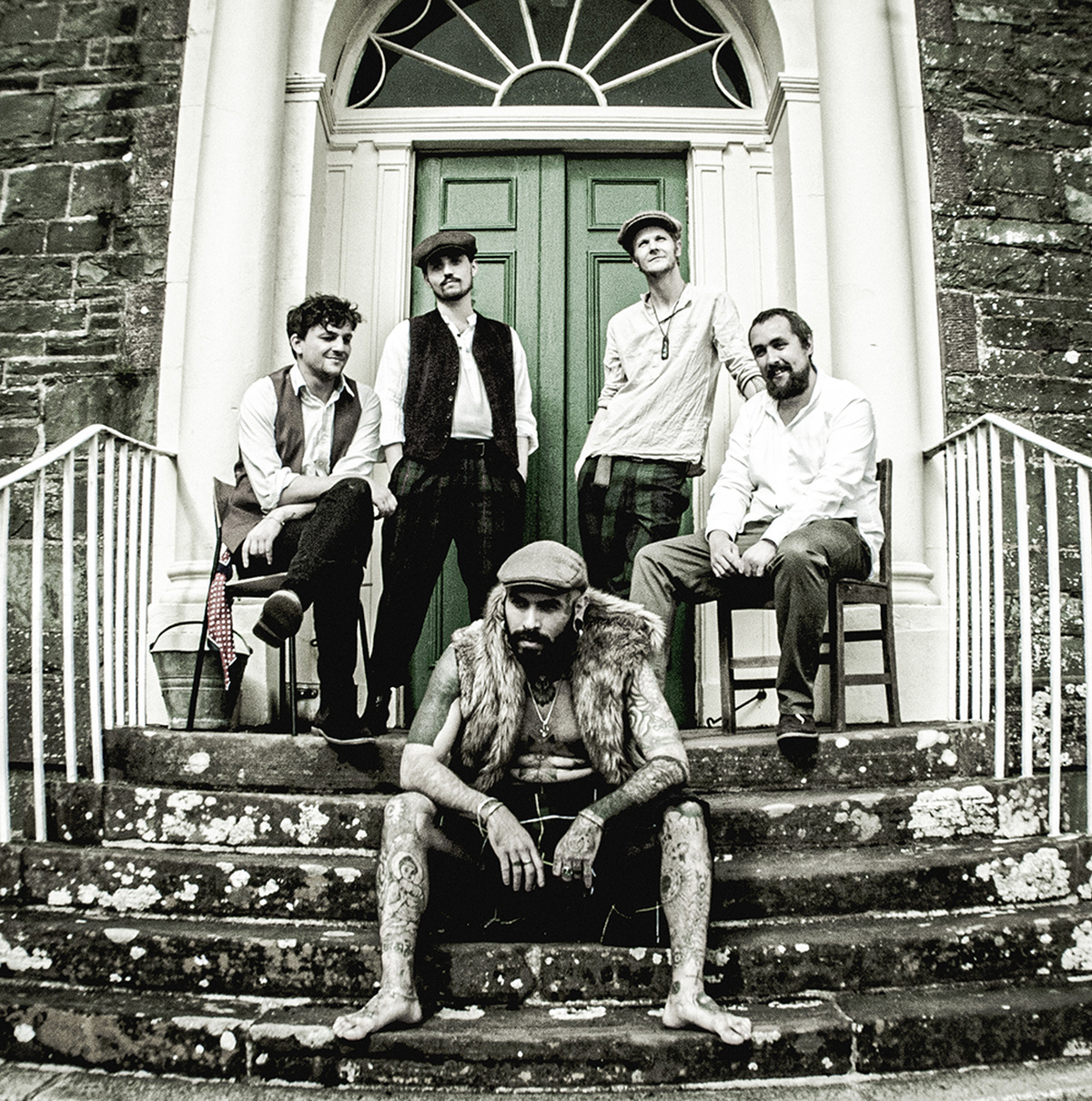 A band photo of An Dannsa Dub, 5 men on the steps of an old brick house all wearing old fashioned garb.