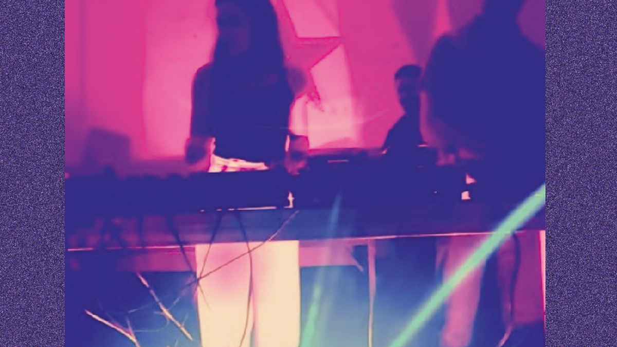 Two DJs stand in purple lighting.