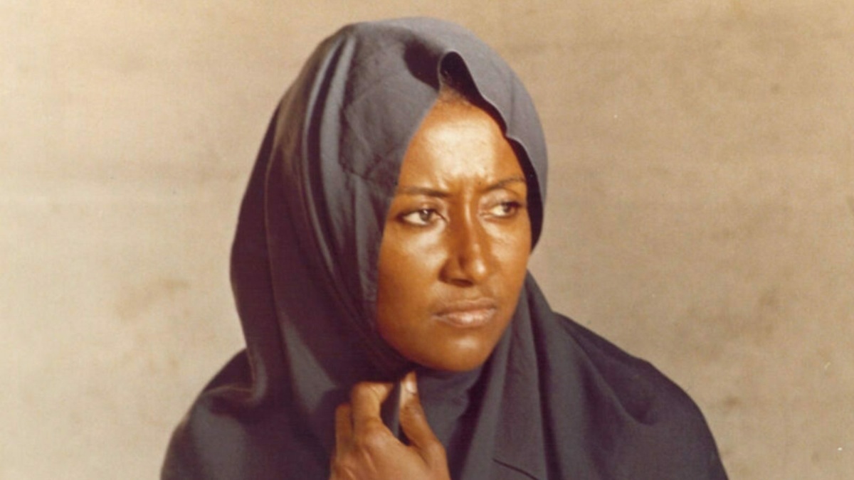 A woman in a head covering looks to the right of the screen she has an intense look on her face.