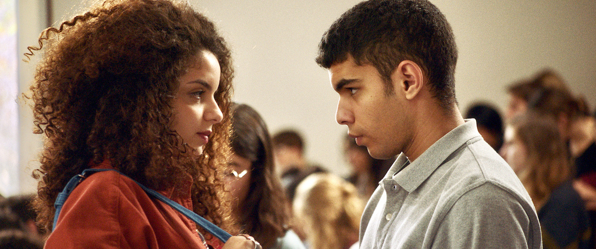 Two young people staring at one another in a crowded room.