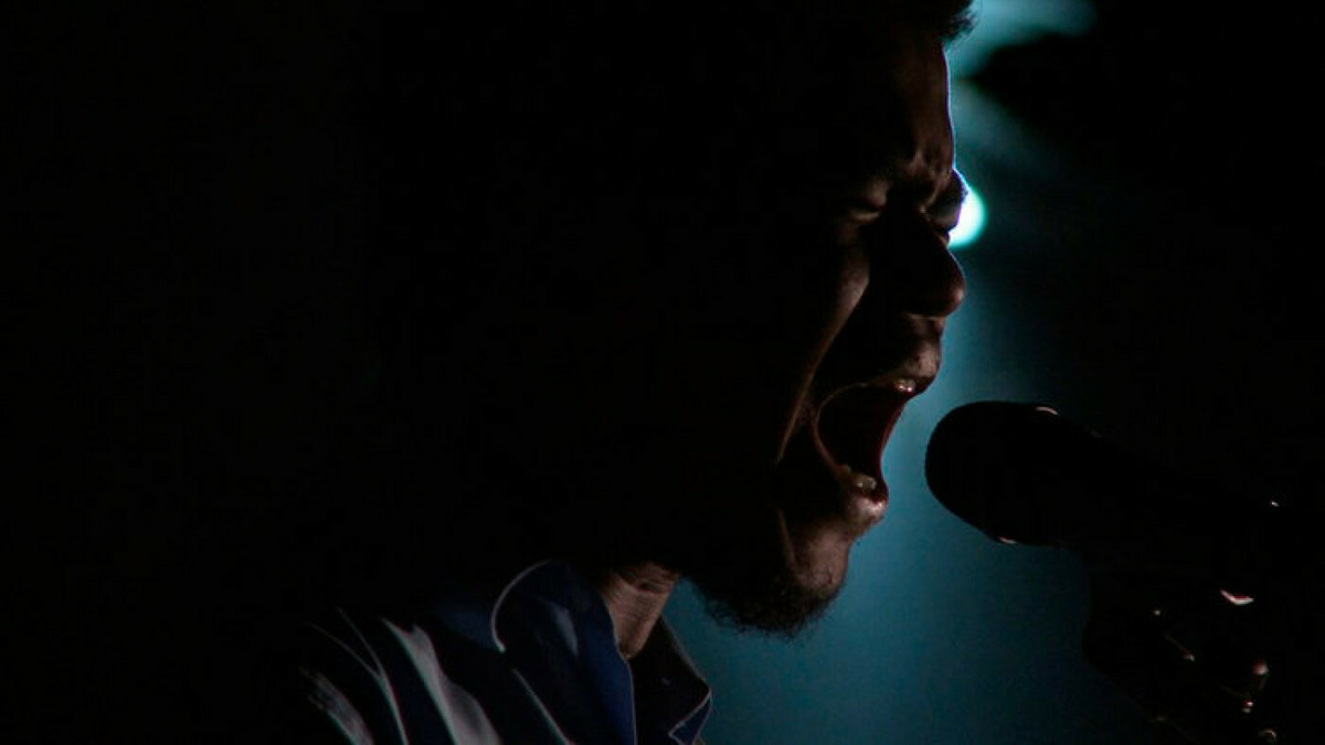 A close-up of a man singing into a microphone in a darkened room.