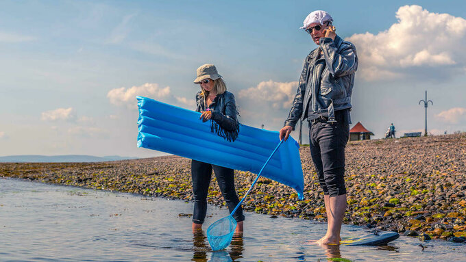 The Vaselines stand at the side of a body of water with a lilo.