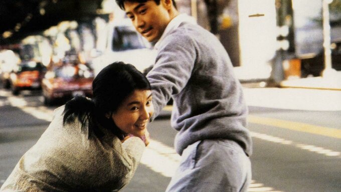 A still from Comrades, Almost a Love Story featuring two people playfully running along a street.