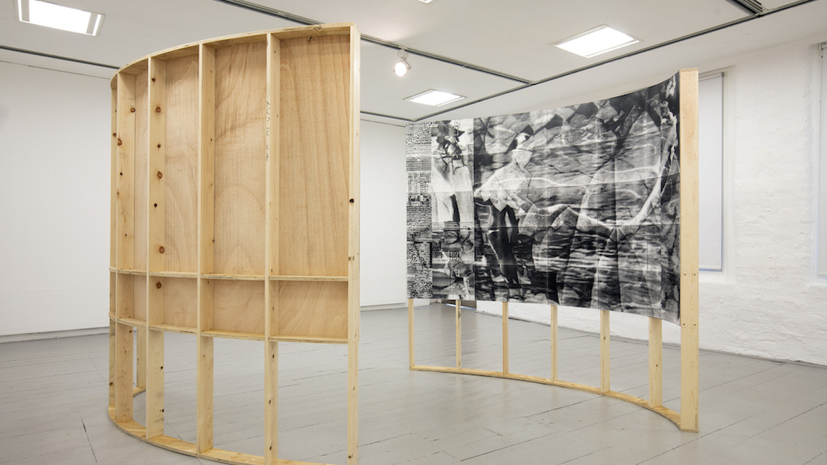 Two large curved structures made from wooden beams face each other in the center of the gallery space.