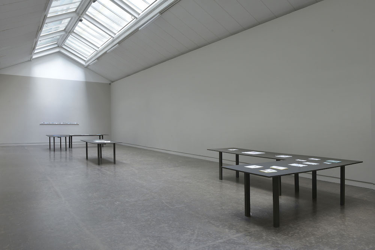 A wide shot of CCA 3, 2 L shaped tables with various pieces of embroidery and documentation sit at each end of the space