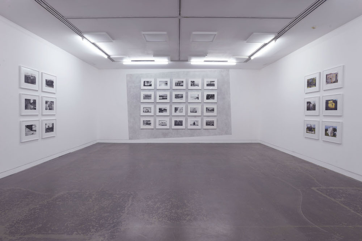 An install in CCA 2 with black and white photos installed on the three walls, with a graphite wall drawing framing some