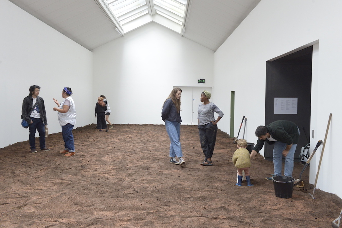 An image of visitors stood in CCA 3 chatting, the floor is covered in cultivated soil.