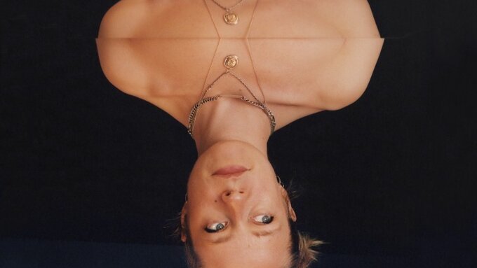 Image of Anna B. Savage's face reflected in what looks like a pool of black liquid, which she seems to be reflected in