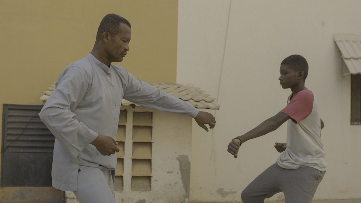 An older man and a young boy face each other, posing as if in dance.