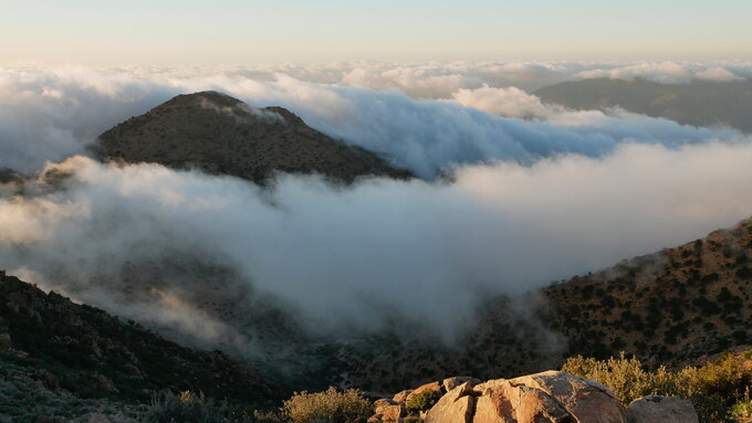 A photograph from a high elevation looking across hilly area shrouded by fog and mist.