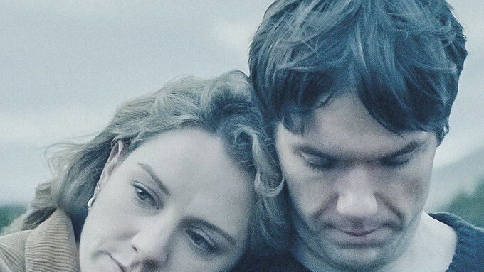 A woman rests her head on a man's shoulder. Both look sad and thoughtful.